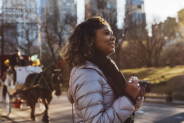 Seitenansicht einer lächelnden Frau mit Digitalkamera in der Hand auf der Straße