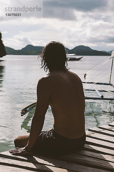 Nachdenklicher Mann ohne Hemd sitzt auf einem Steg über dem Meer