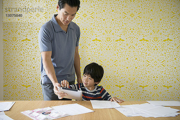 Vater hilft dem Jungen bei den Hausaufgaben durch Tablette zu Hause
