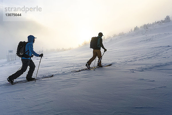 Männliche Freunde gehen bei Nebel auf schneebedecktem Feld