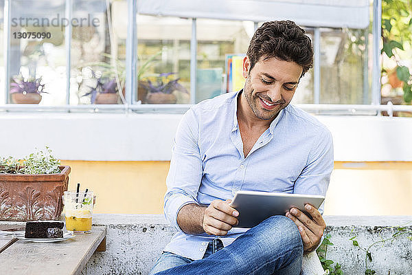 Lächelnder Mann benutzt Tablet-Computer  während er im Straßencafé sitzt