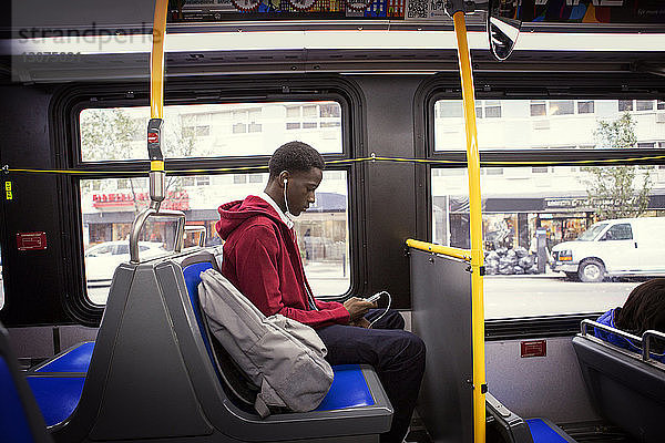 Seitenansicht eines Studenten  der während einer Busfahrt Musik hört