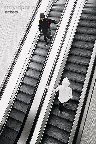 Hochwinkelansicht eines Mannes und einer Frau mit Kapuzenhemden  die auf Rolltreppen gehen