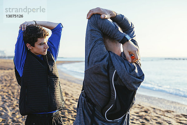Vater und Sohn strecken die Arme aus  während sie einander am Strand gegenüberstehen