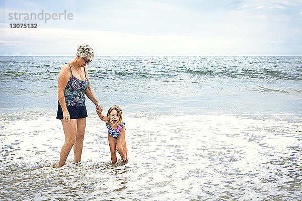 Verspieltes Mädchen mit Großmutter  die am Strand am Ufer im Wasser steht