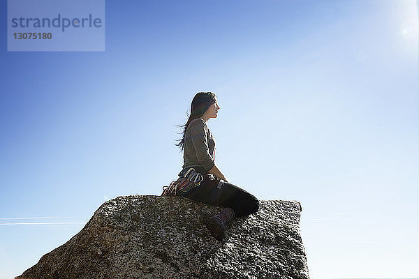 Seitenansicht einer Frau  die auf einem Felsen gegen den Himmel sitzt