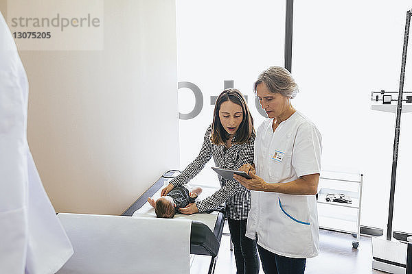 Arzt zeigt Frau mit kleinem Jungen im Krankenhaus einen Tablet-Computer