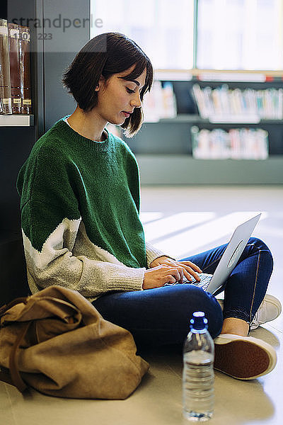 Frau benutzt Laptop-Computer  während sie in der Bibliothek auf dem Boden sitzt
