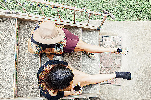 Draufsicht auf Freundinnen  die Kaffee trinken  während sie auf Stufen sitzen