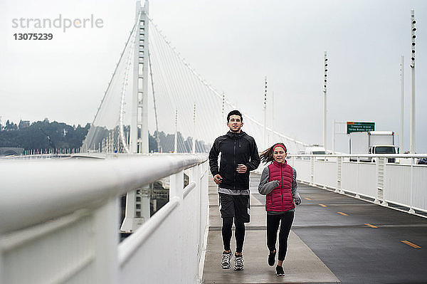 Porträt von entschlossenen Athleten  die auf der Bay Bridge gegen den Himmel laufen