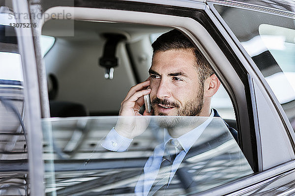 Geschäftsmann schaut weg  während er ein Smartphone im Auto benutzt