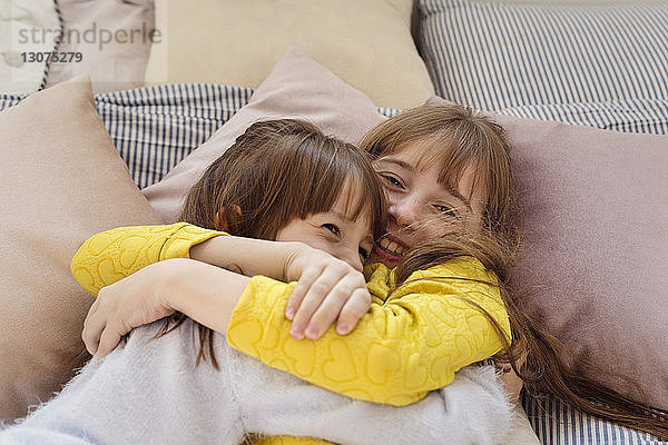 Draufsicht auf Schwestern  die sich umarmen  während sie zu Hause auf dem Bett liegen