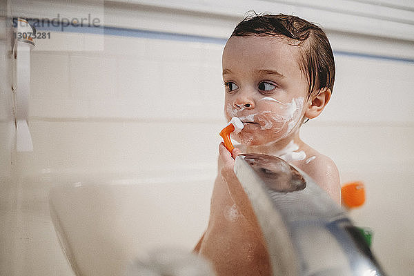 Junge ohne Shirt rasiert sich beim Baden in der Badewanne zu Hause