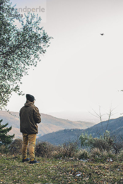 Rückansicht eines männlichen Wanderers  der einen Quadcopter fliegt  während er auf einem Berg vor klarem Himmel steht