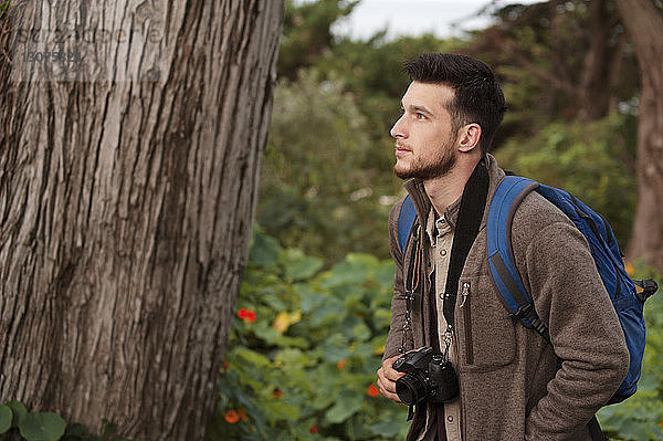 Männlicher Wanderer schaut weg  während er im Wald eine Kamera hält