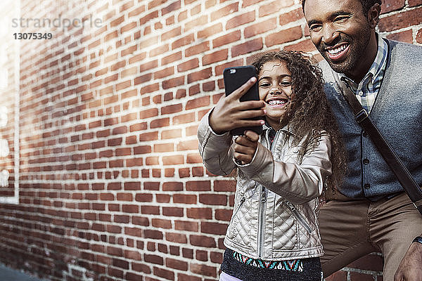 Tochter nimmt Selfie mit Vater durch Smartphone an Ziegelmauer