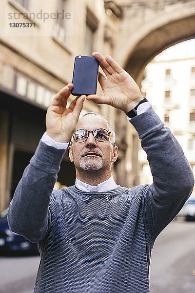 Mann fotografiert mit Smartphone im Stehen in der Stadt