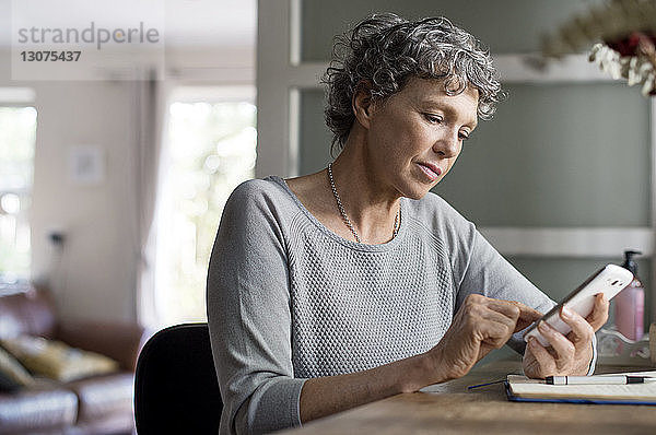 Reife Frau benutzt Smartphone bei der Arbeit zu Hause