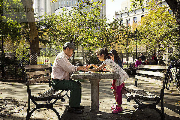 Seitenansicht von Mädchen beim Damespiel mit dem Großvater am Tisch im Park