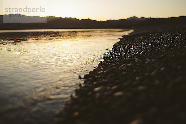 Nahaufnahme von Kieselsteinen am Seeufer gegen Berge bei Sonnenuntergang