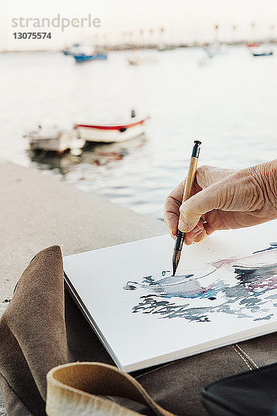 Ausschnitt einer Frau  die auf Papier malt  mit Booten  die auf See festgemacht sind