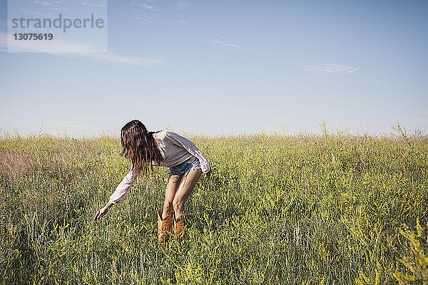 Frau berührt Gras auf Feld gegen Himmel
