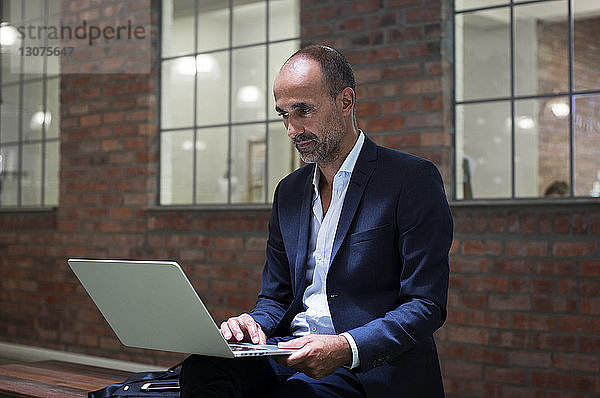 Geschäftsmann benutzt Laptop-Computer  während er auf einem Sitz gegen ein Büro sitzt