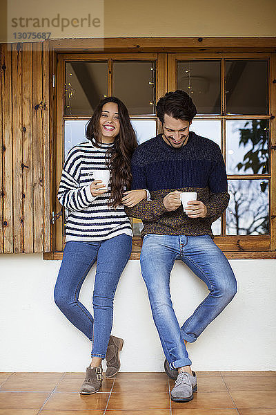 Glückliches Paar trinkt Kaffee  während es am Fenster auf der Veranda steht