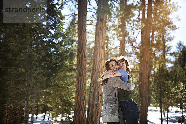 Fröhliche Freunde umarmen sich  während sie im Winter im Wald stehen