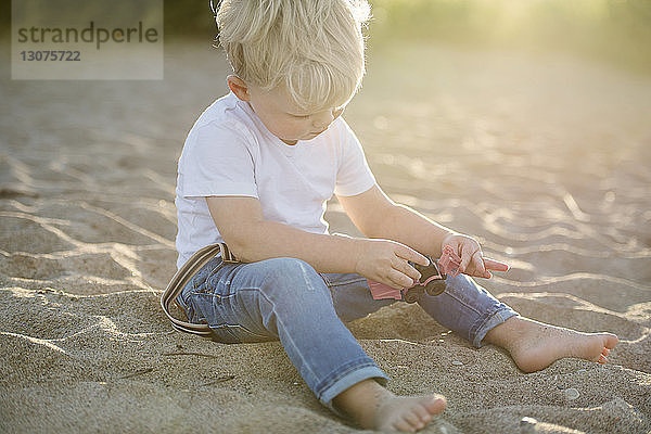 Kleiner Junge spielt mit Spielzeug  während er am Strand im Sand sitzt