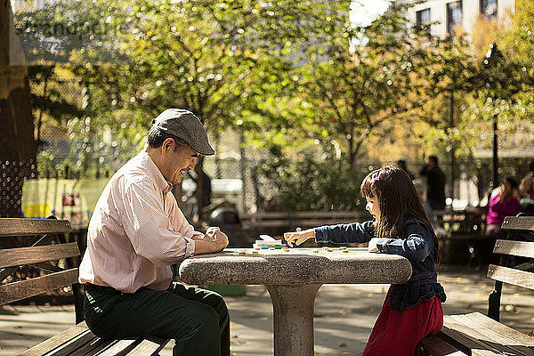 Großvater und Enkelin spielen Brettspiel  während sie im Park am Tisch sitzen