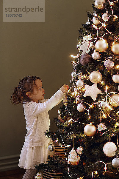 Mädchen schmückt den Weihnachtsbaum zu Hause