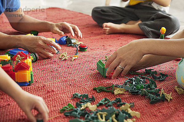 Ausgeschnittenes Bild einer Familie  die zu Hause mit Spielzeug auf dem Boden spielt