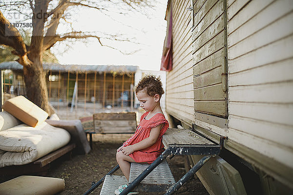 Seitenansicht eines süßen Mädchens  das auf Metallstufen auf einem Bauernhof sitzt