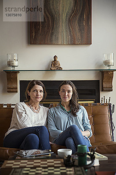 Porträt einer lächelnden Tochter und Mutter  die auf dem Sofa im Wohnzimmer sitzen