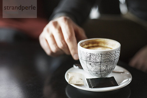 Ausgeschnittenes Bild eines Geschäftsmannes  der in einem Café eine Kaffeetasse am Tisch hält