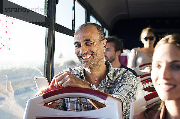 Glücklicher Mann benutzt Mobiltelefon während der Fahrt im Reisebus