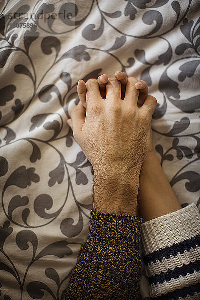 Ausgeschnittenes Bild eines Paares  das zu Hause am Bett Händchen hält