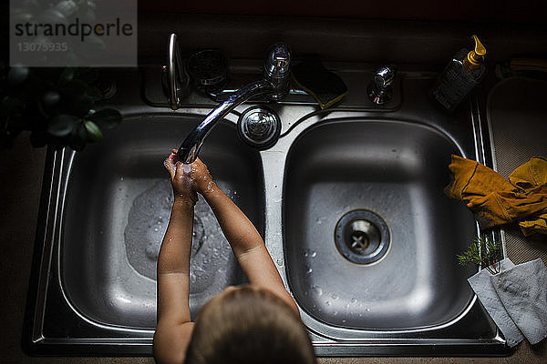 Schrägaufnahme eines Jungen  der sich zu Hause in der Spüle die Hände wäscht