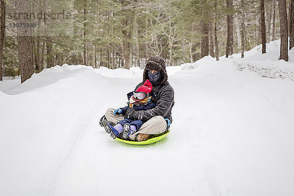 Vater sitzt mit Tochter auf Schlitten auf schneebedecktem Feld