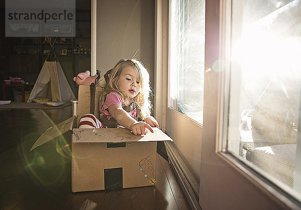 Süßes Mädchen sitzt zu Hause in einem Pappkarton an der Tür