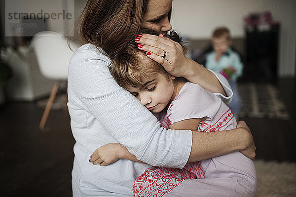 Mutter umarmt Mädchen  während sie zu Hause auf dem Boden sitzt