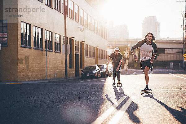 Freunde skateboarden bei Sonnenschein auf der Stadtstraße gegen den Himmel