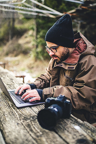 Männlicher Wanderer mit Laptop-Computer und Kamera auf Tisch im Wald