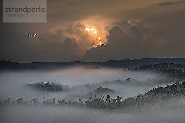 Blitzwolken über Wald und Berg bei Nacht