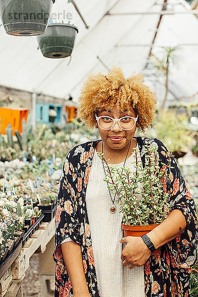 Porträt einer Frau  die eine Topfpflanze hält  während sie in der Gärtnerei steht
