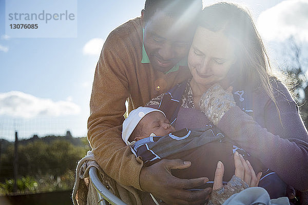 Mutter und Vater umarmen Kleinkind an einem sonnigen Tag gegen den Himmel