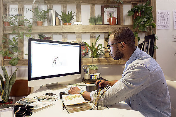 Seitenansicht eines männlichen Illustrators  der im Kreativbüro am Computer malt