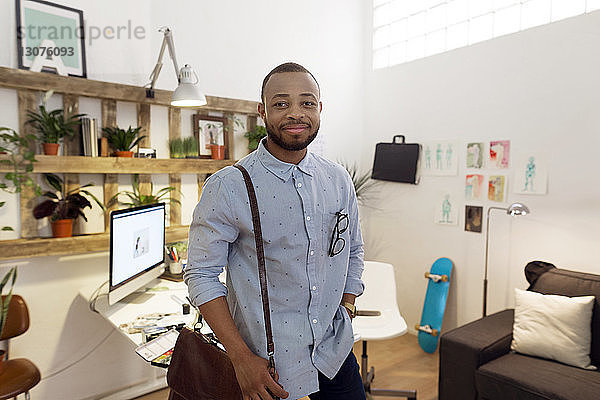 Porträt eines lächelnden männlichen Illustrators  der eine Tasche trägt  während er im Kreativbüro steht