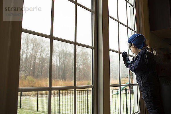 Zu Hause stehender Junge schaut durchs Fenster